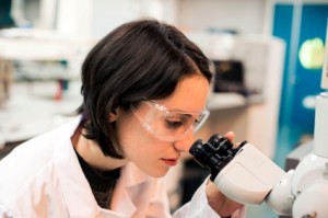 rol de científico, una mujer con máscara mira por un microscopio
